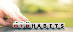 Hand flipping letter blocks to change the word “old habits” to “new habits,” symbolizing behavior change and habit formation