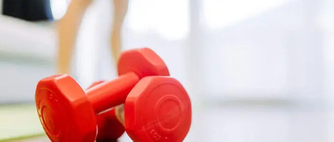 red dumbbells sitting on a hardwood floor with blurred image of legs in the background.