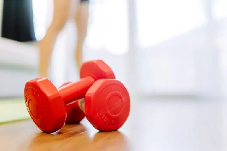 red dumbbells sitting on a hardwood floor with blurred image of legs in the background.