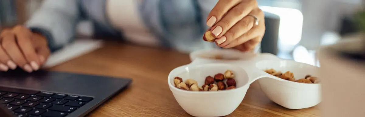 woman snacking on mixed nuts while working on her computer