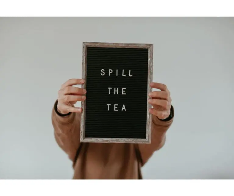 person holding a sign that says "spill the tea"