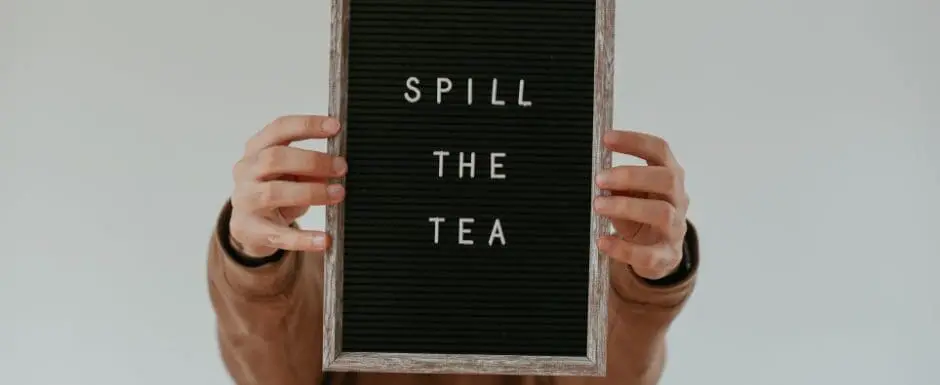 person holding a sign that says "spill the tea"