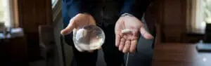 A person's hands holding a clear, inflated spherical gastric balloon in one hand and its uninflated, swallowable white capsule form with an attached thin tube in the other.