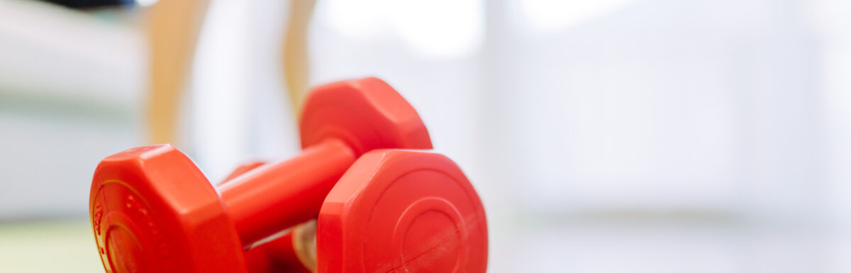 red dumbbells sitting on a hardwood floor with blurred image of legs in the background.
