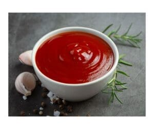 Bowl of sauce sitting on a table top with a clove of garlic and sprig of rosemary