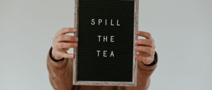 person holding a sign that says "spill the tea"