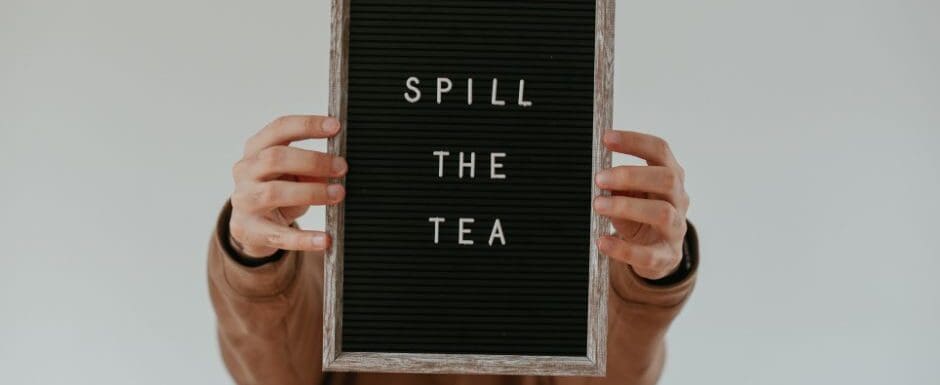 person holding a sign that says "spill the tea"